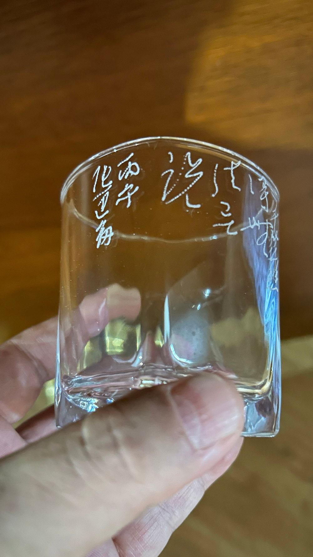 Hand‑held close‑up displaying full wrapped‑around calligraphy carving on glass side
