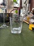 Full shot of square hand‑engraved calligraphy tumbler glass placed on green fabric table surface