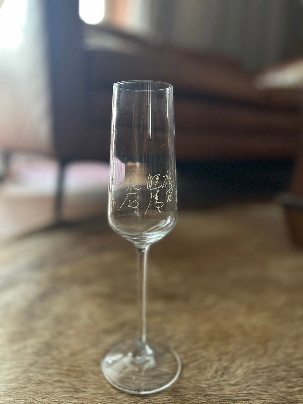 Full product shot of complete tall stemmed wine flute on textured background, showing overall silhouette and engraved verse
