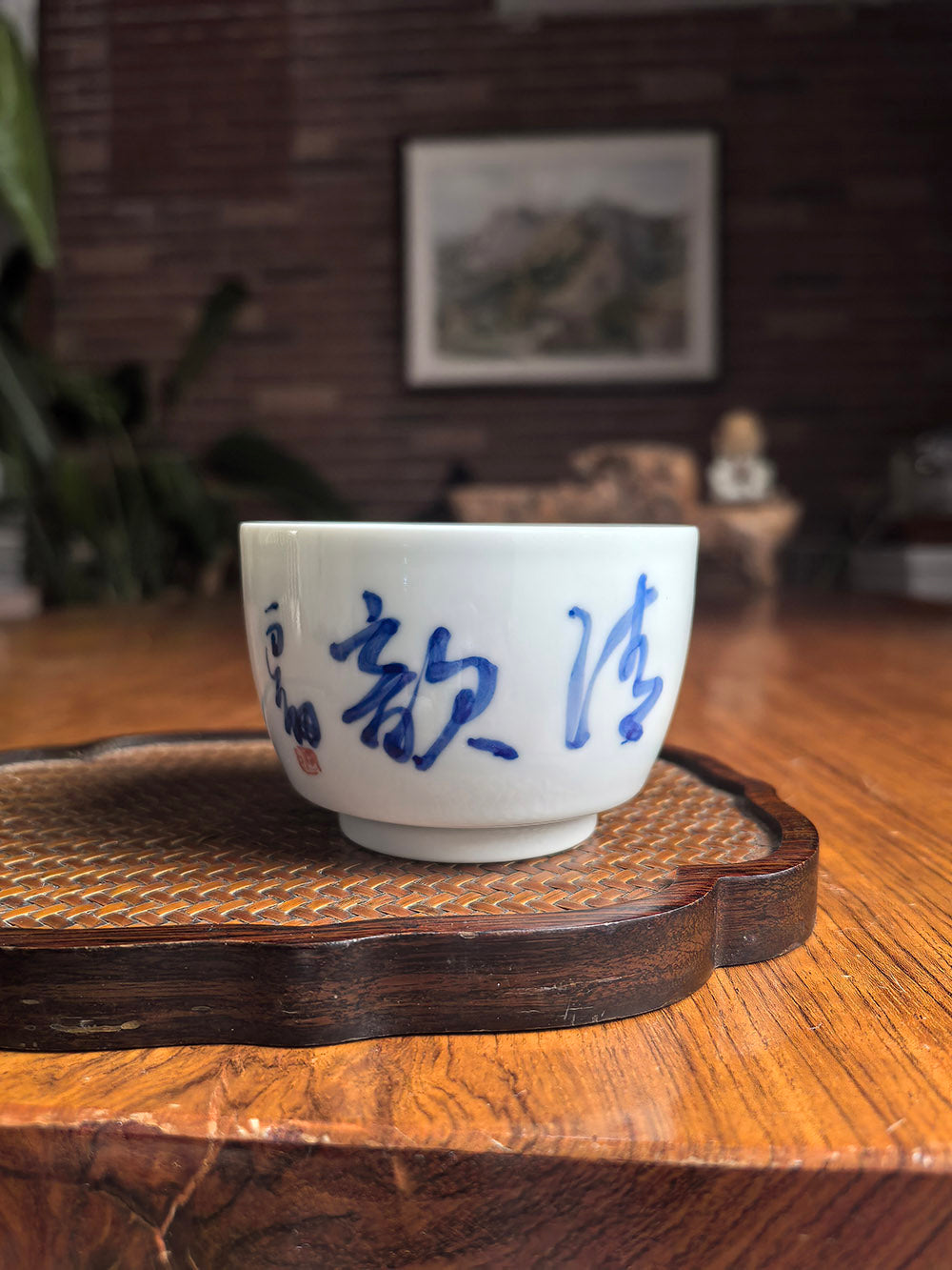 Hand-thrown Jingdezhen qingbai porcelain folded-base tea cup with "Orchid's Grace" calligraphy, placed on a wooden tea table with bamboo mat background