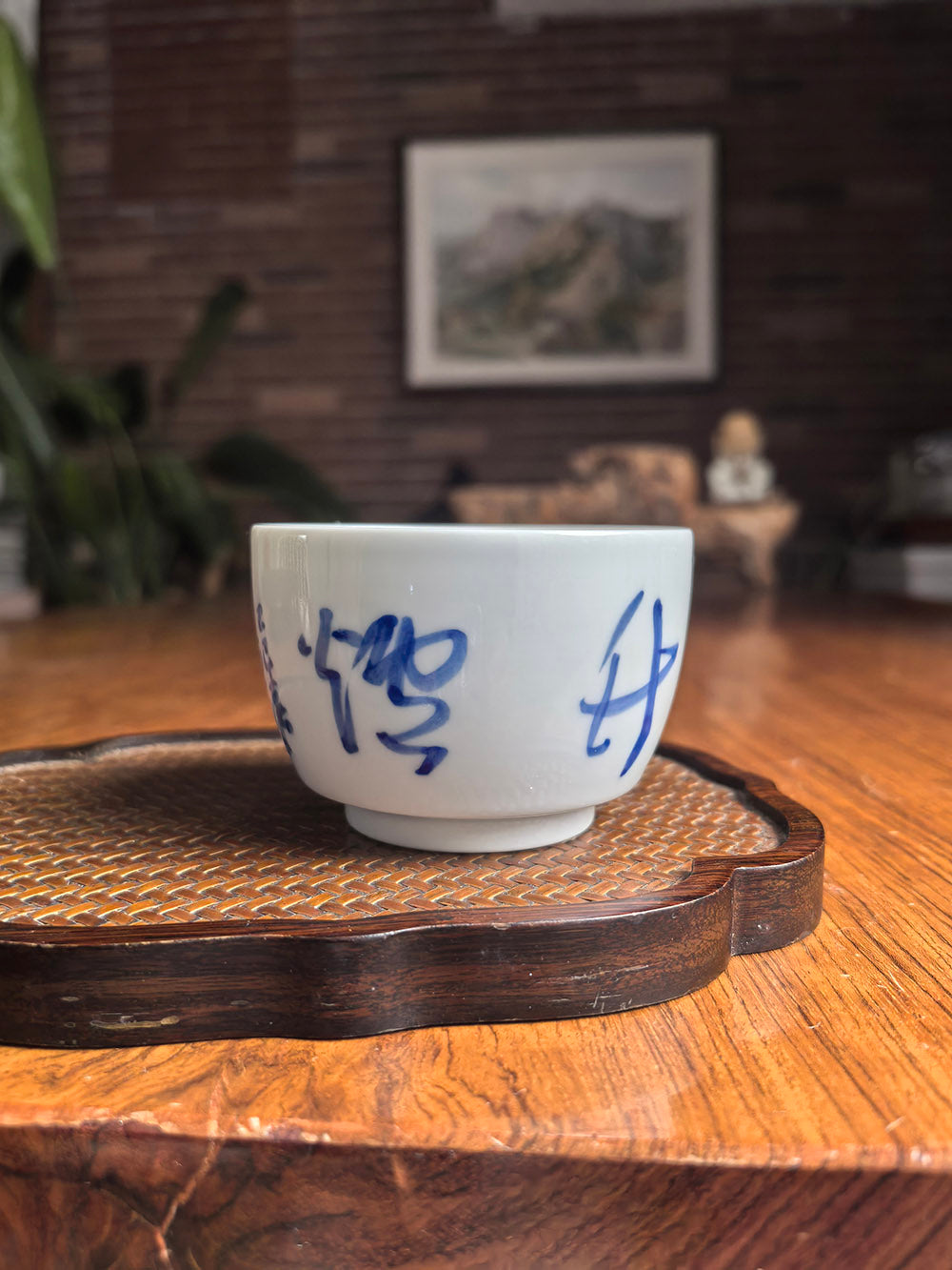 Hand-thrown Jingdezhen qingbai porcelain folded-base tea cup with "Pine Wind Bamboo Stove" calligraphy, placed on a woven bamboo mat in a traditional zen tea setting with wooden background