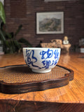 Hand-thrown Jingdezhen qingbai porcelain folded-base tea cup with Du Fu "Spring Rain" calligraphy poem, placed on a dark wood tea table with bamboo whisk background