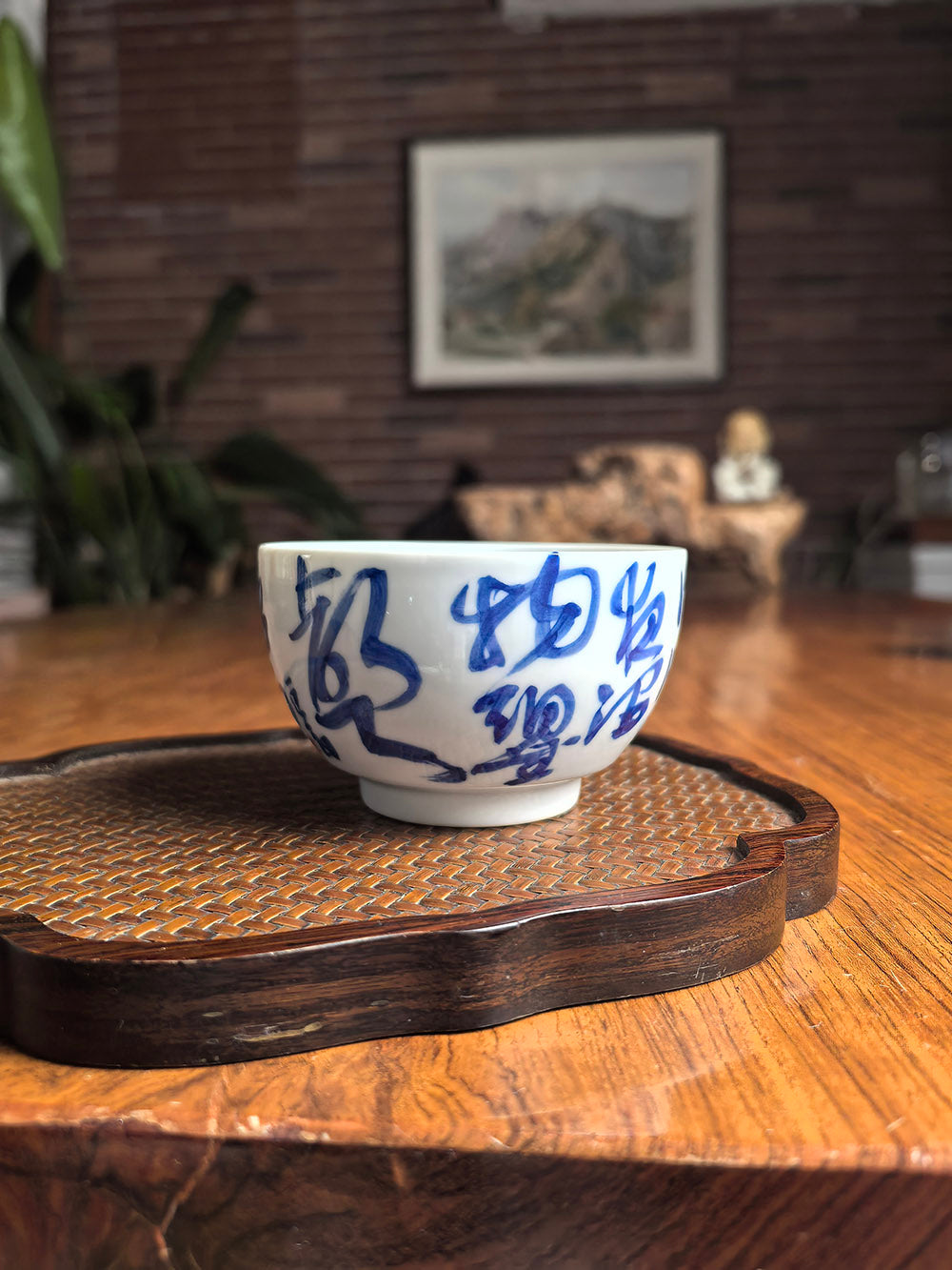 Hand-thrown Jingdezhen qingbai porcelain folded-base tea cup with Du Fu "Spring Rain" calligraphy poem, placed on a dark wood tea table with bamboo whisk background
