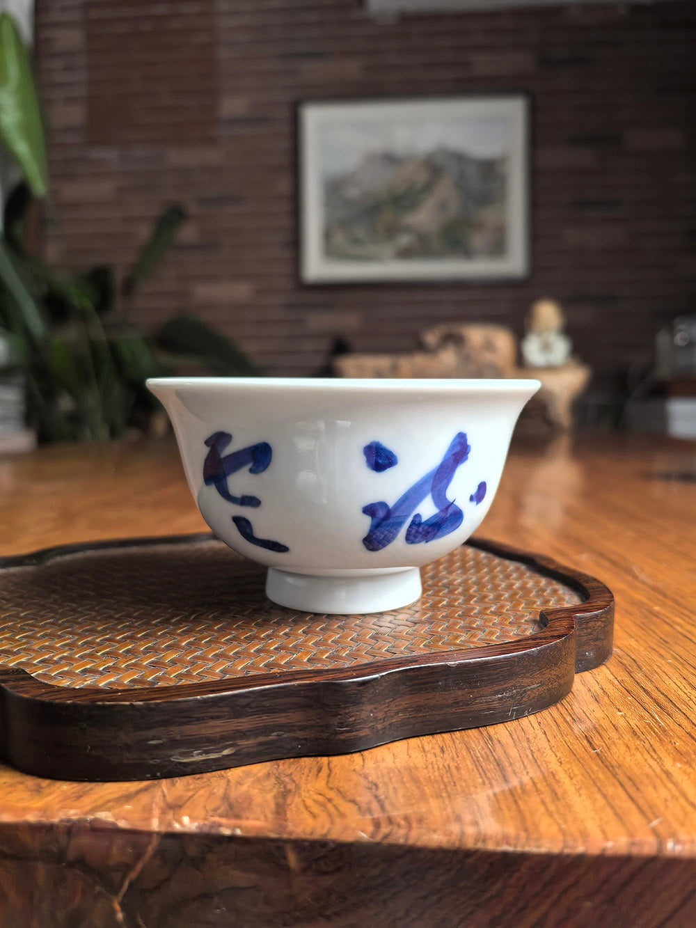 Hand-thrown Jingdezhen qingbai porcelain press-hand tea cup with "Flowing Clouds and Moonlight" calligraphy, placed on a dark wood tea table with bamboo mat background