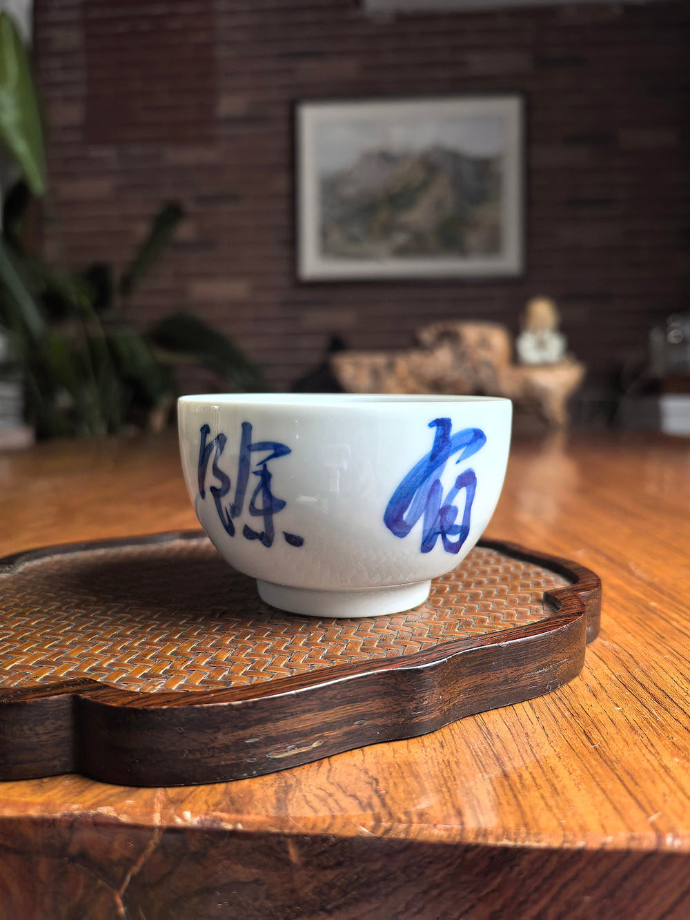 Hand-thrown Jingdezhen qingbai porcelain folded-base tea cup with "Abundance" calligraphy, placed on a dark wood tea table with bamboo whisk background