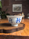 Hand-thrown Jingdezhen qingbai porcelain press-hand tea cup with "Planting Bamboo to Observe Vitality" calligraphy, placed on a dark wood tea table with bamboo whisk background