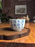 Hand-thrown Jingdezhen qingbai porcelain folded-base tea cup with Wang Xizhi "Timely Clear Weather" calligraphy, placed on a dark wood tea table with bamboo whisk background