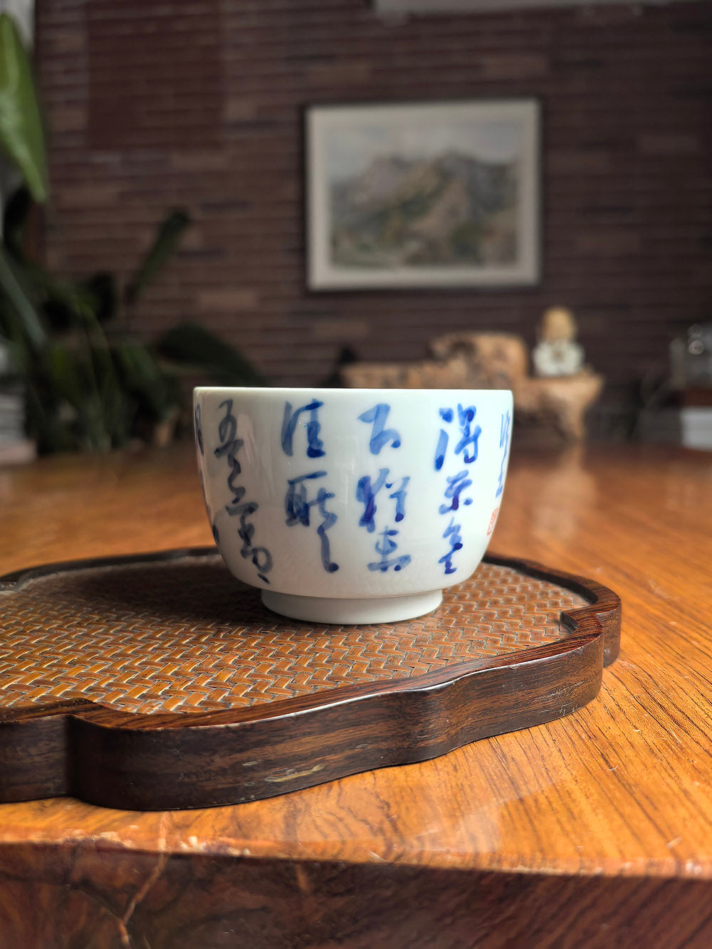 Hand-thrown Jingdezhen qingbai porcelain folded-base tea cup with Wang Xizhi "Timely Clear Weather" calligraphy, placed on a dark wood tea table with bamboo whisk background