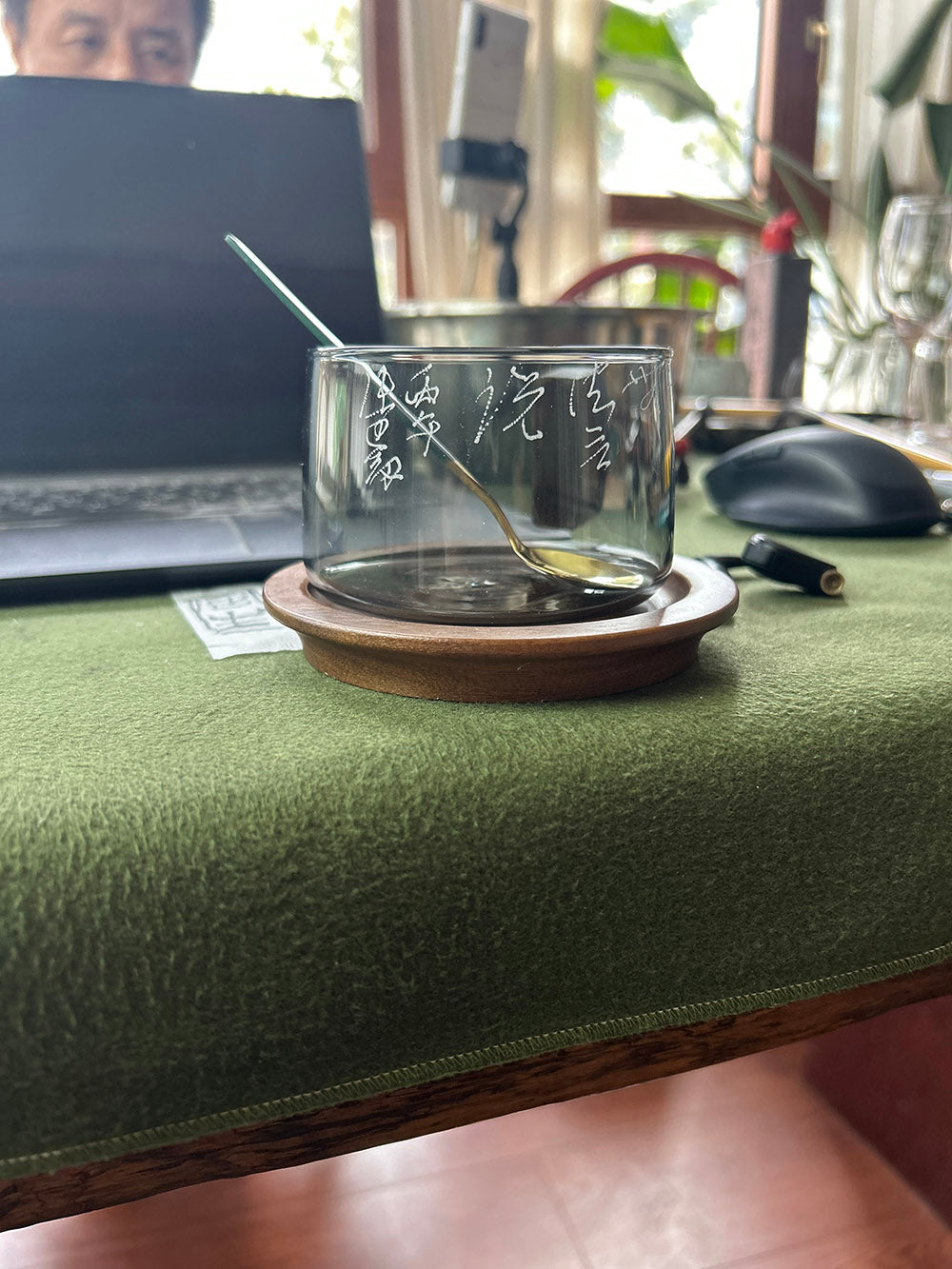 Side view of glass mug displaying hand‑frosted calligraphy engraving without handle, placed on wooden coaster